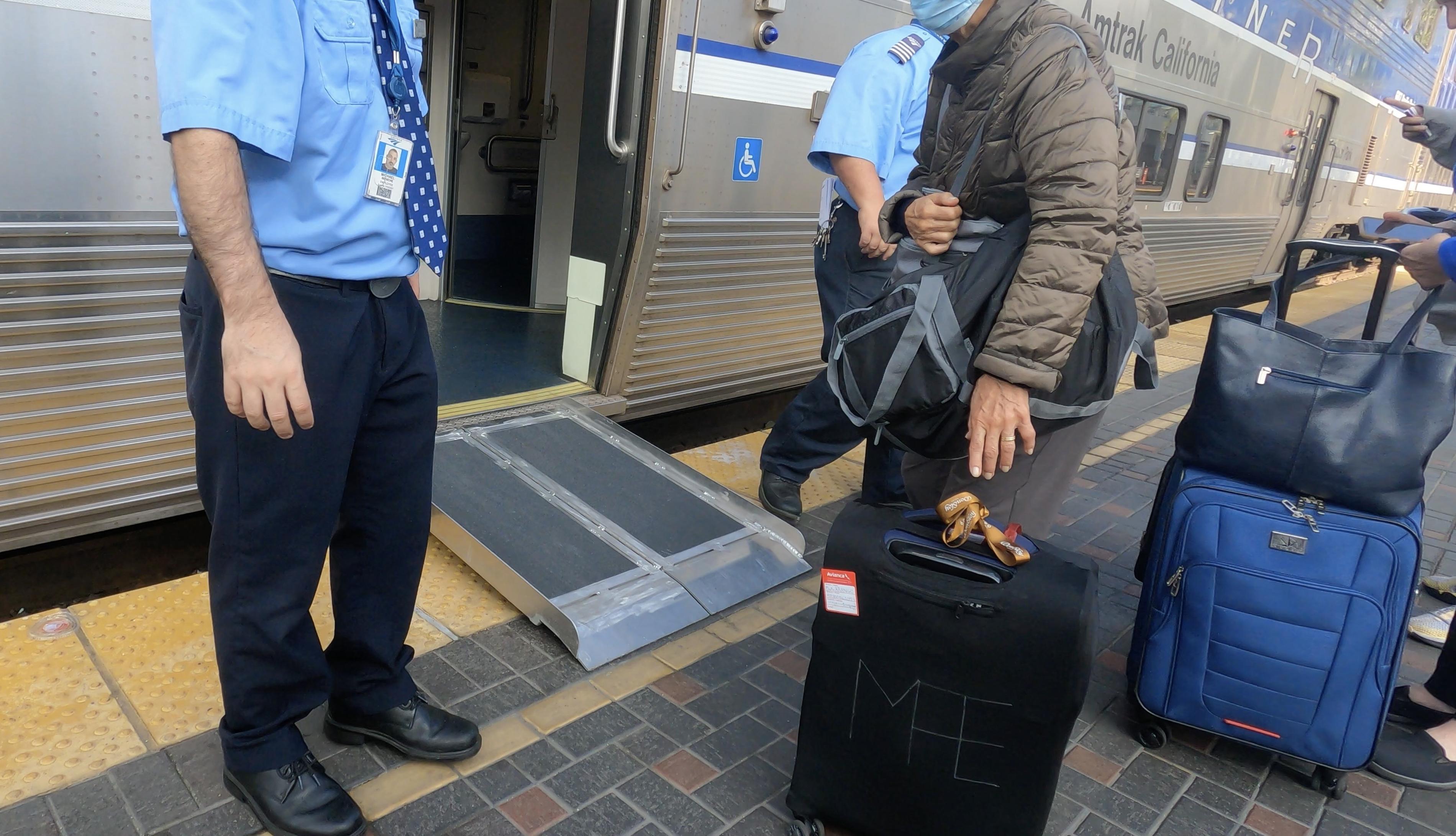 People with their rolling luggage crowd around the ramp to board before Aubrie can. The conductors stand to the side.